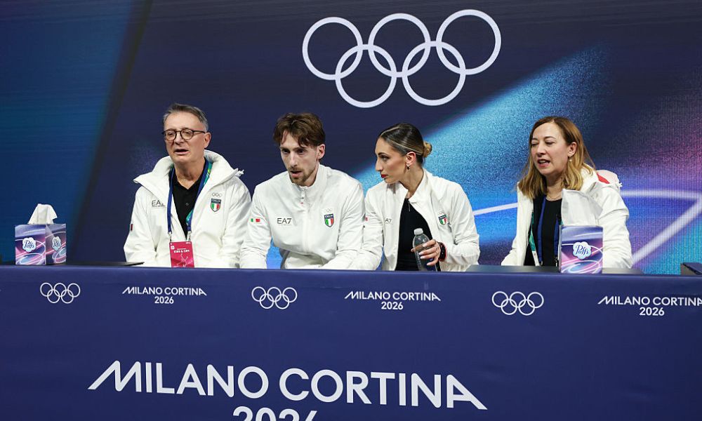 Anne-Sophie Voumard speaking at a press conference in Milan with TOP partner logos displayed behind her.